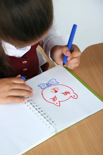 Beautiful little schoolgirl in classroom and draws in notebook — Stock Photo, Image