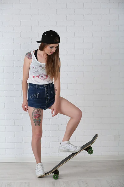 Menina hipster bonita com skate no fundo claro — Fotografia de Stock