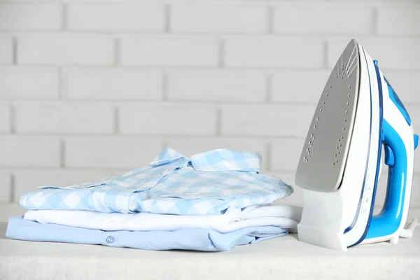 Pile of clothes and electric iron on brick wall background — Stock Photo, Image