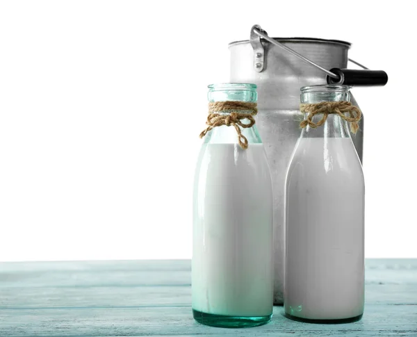 Ретро банка для молока и стеклянных бутылок молока на деревянном столе, на белом фоне — стоковое фото
