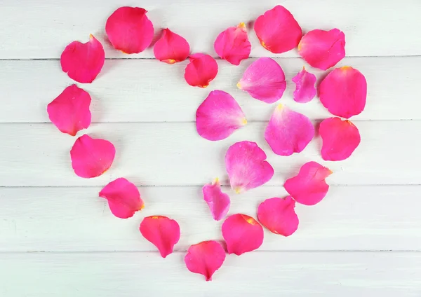 Corazón de pétalos de rosa sobre fondo de madera — Foto de Stock