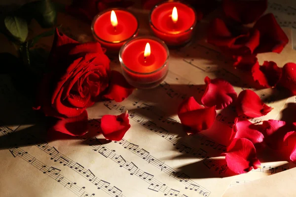 Mooie roze bloemblaadjes met kaarsen op muziek bladen, close-up — Stockfoto