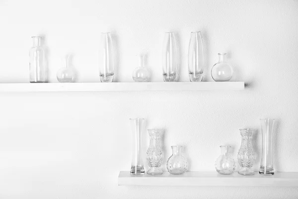 Vasos de vidro decorativos na prateleira de madeira no fundo papel de parede branco — Fotografia de Stock