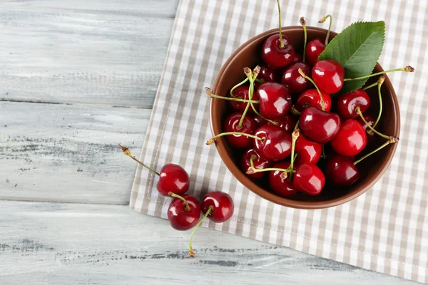 Cerezas frescas en tazón con servilleta en mesa de madera, primer plano — Foto de Stock