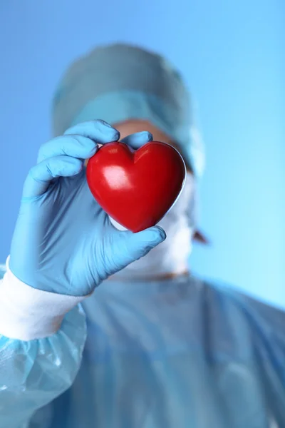 Médico segurando coração decorativo no fundo azul — Fotografia de Stock