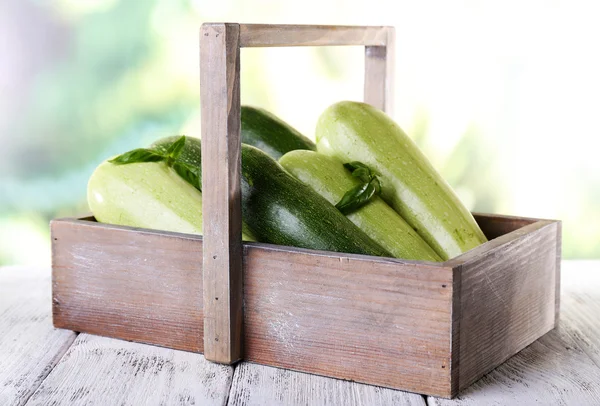 Frische Zucchini mit Kürbis und Basilikum in Holzkiste auf hellem Hintergrund — Stockfoto