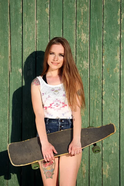 Fata frumoasa cu corp tatuat, tinand skateboard pe fundal de perete din lemn — Fotografie, imagine de stoc