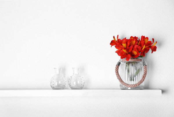 Decorative glass vases with flowers  on wooden shelf  on white wallpaper background