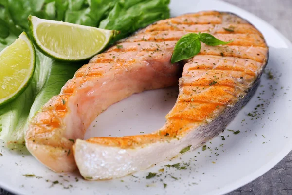 Tasty grilled salmon with lime and lettuce on table close up — Stock Photo, Image