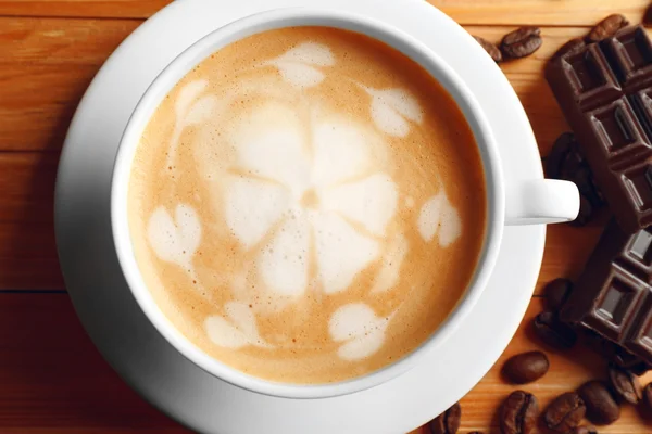 Tasse Kaffee Latte Art mit Körnern und Schokoriegel auf Holztisch, Nahaufnahme — Stockfoto