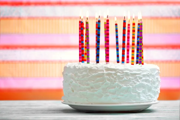 Verjaardagscake met kaarsen op kleurrijke gestreepte achtergrond — Stockfoto