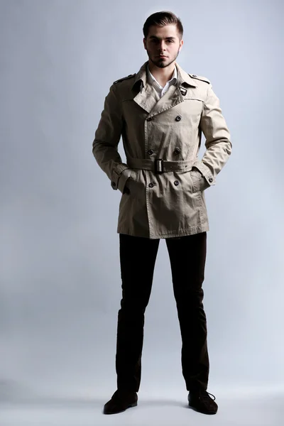 Młody mężczyzna w płaszczu na szarym tle — Zdjęcie stockowe