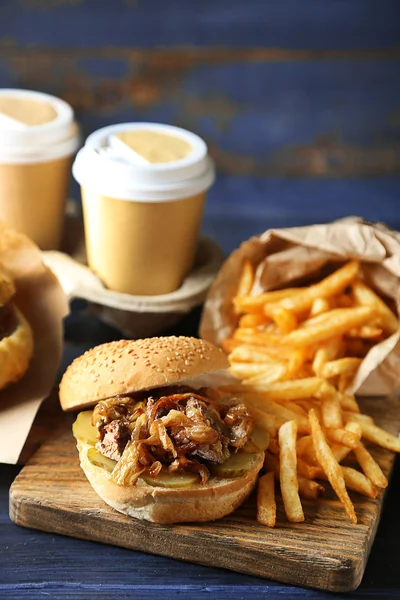 Tasty burger and french fries on plate, on wooden table background. Unhealthy food concept — Stock Photo, Image