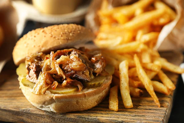 Hambúrguer saboroso e batatas fritas no prato, no fundo da mesa de madeira. Conceito alimentar pouco saudável — Fotografia de Stock