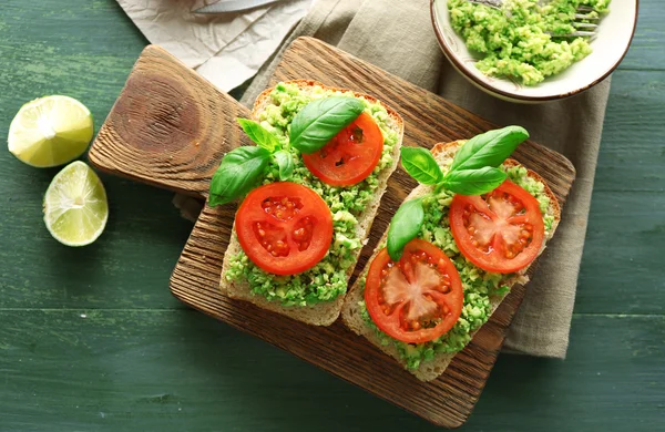 Panino vegano con avocado e verdure sul tagliere, su fondo di legno — Foto Stock