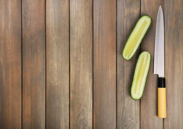 Halves of cucumber with knife on wooden background — Stock Photo, Image
