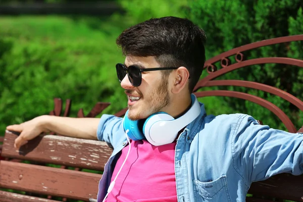 Homem com fones de ouvido descansando no banco no parque — Fotografia de Stock