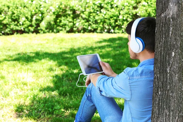 Man with headphones resting under tree in park — Stock Photo, Image