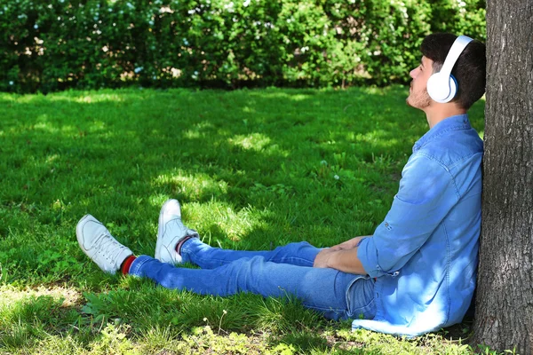 Man met hoofdtelefoon rusten onder boom in het park — Stockfoto