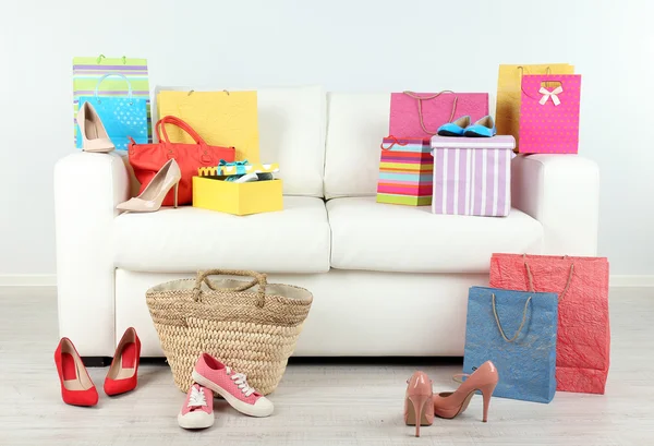 Heap of shopping bags with boxes and shoes on sofa in room — Stock Photo, Image