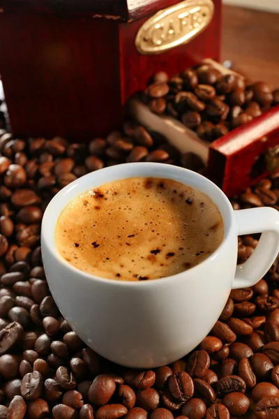 Xícara de café fresco com grãos na mesa, close-up — Fotografia de Stock
