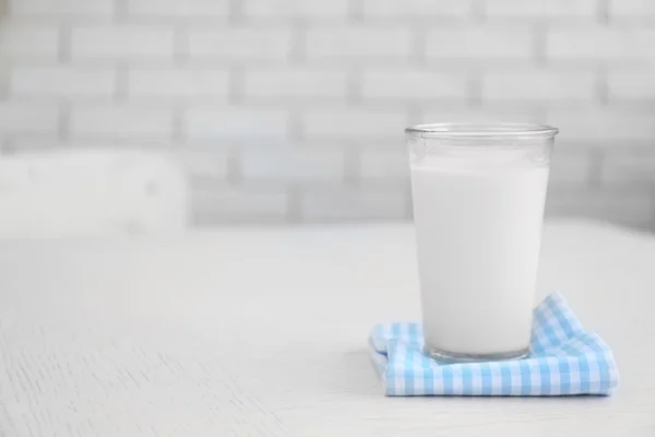 Vidro de leite na mesa de madeira, no fundo da parede de tijolos — Fotografia de Stock