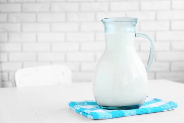 Milchkrug auf Holztisch, auf Ziegelwand Hintergrund — Stockfoto