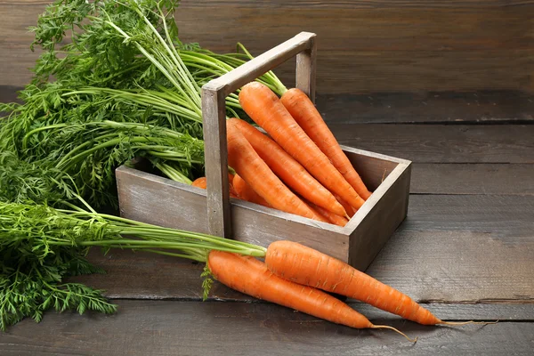 Fresh organic carrots in crate on wooden background — Stock Photo, Image
