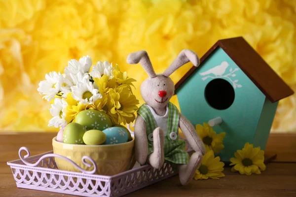 Paashaas met beschilderde Pasen eieren met bloemen op houten tafel op gele achtergrond — Stockfoto