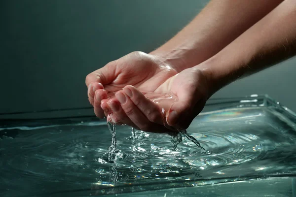 Mains féminines avec éclaboussures d'eau sur fond sombre — Photo