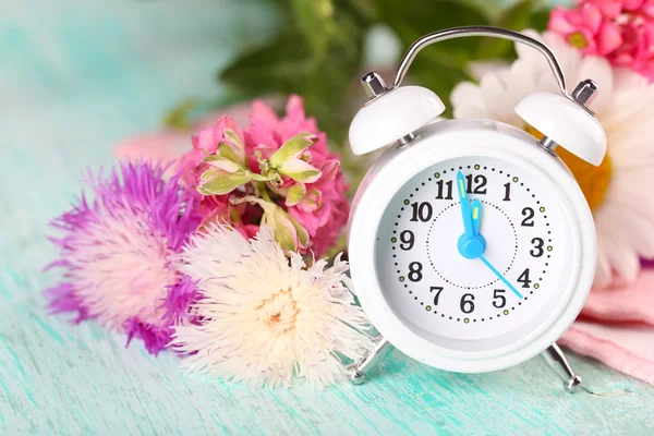 Liten väckarklocka med vackra blommor på bordet på nära håll — Stockfoto