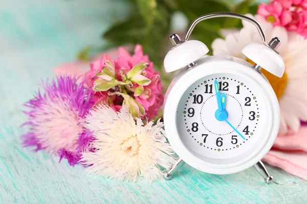 Pequeño despertador con hermosas flores en la mesa de cerca —  Fotos de Stock