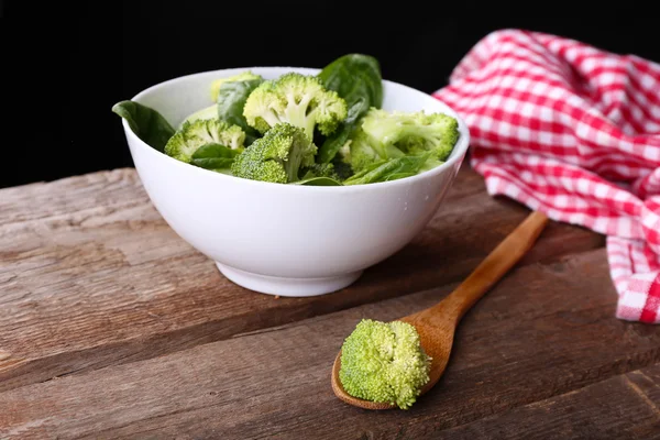 Färsk broccoli med spenat i skål på träbord nära håll — Stockfoto