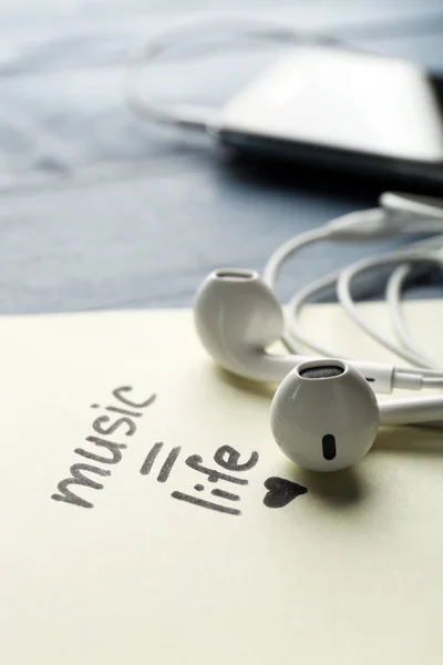 Earphones with text Music - life on sticker on wooden table, closeup — Stock Photo, Image
