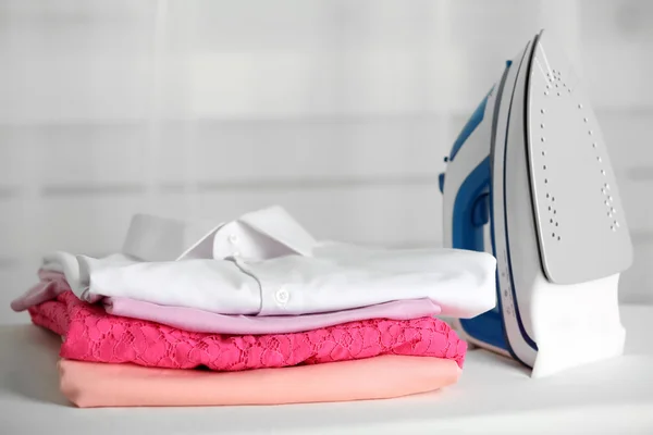 Pile of clothes and electric iron — Stock Photo, Image