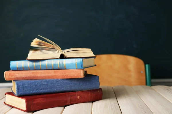 Pilha de livros na mesa, no fundo do quadro negro — Fotografia de Stock