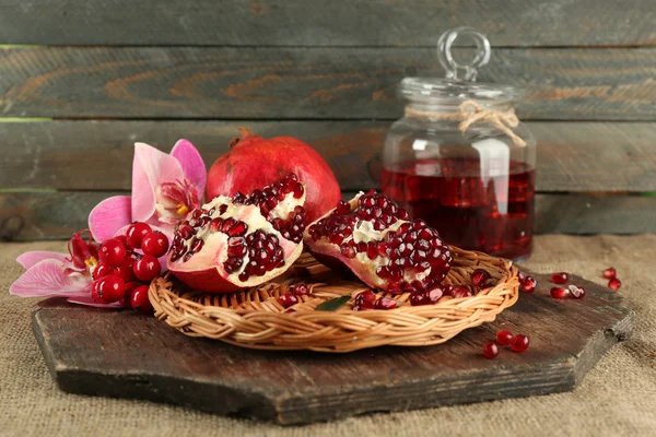 Pomegranate seeds on wicker tray and jar of juice on wooden background