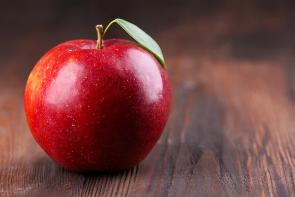 Czerwone jabłko z liściem na drewnianym stole, zbliżenie — Zdjęcie stockowe