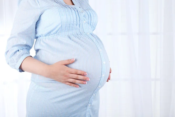 Vacker ung gravid kvinna röra hennes mage på ljus bakgrund — Stockfoto