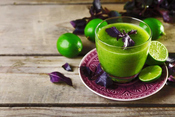Стакан зеленого здорового сока с базиликом и лаймами на столе — стоковое фото