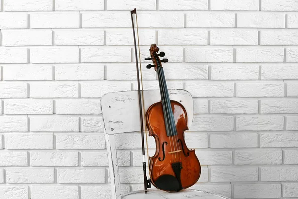 Скрипка на стуле, на кирпичном фоне стены — стоковое фото