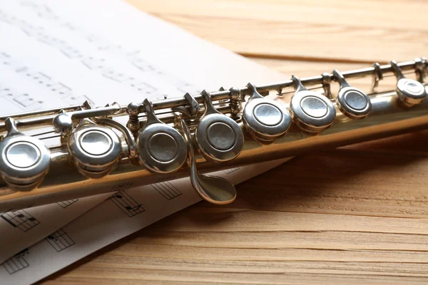 Silver flute with music notes on wooden table close up — Stock Photo, Image