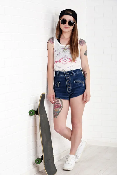 Menina hipster bonita com skate no fundo claro — Fotografia de Stock