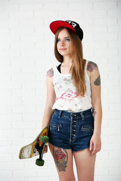 Schöne Hipster-Mädchen mit Skateboard auf hellem Hintergrund — Stockfoto