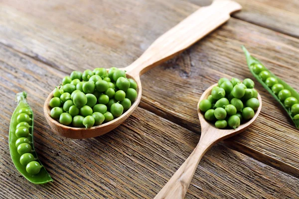 Guisantes verdes frescos en cuchara de madera en la mesa de cerca — Foto de Stock