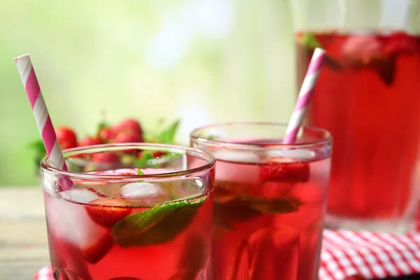 Jarra completa y vasos de jugo de fresa con bayas sobre fondo brillante — Foto de Stock