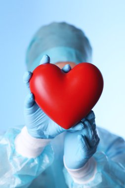 Doctor holding decorative heart on blue background clipart
