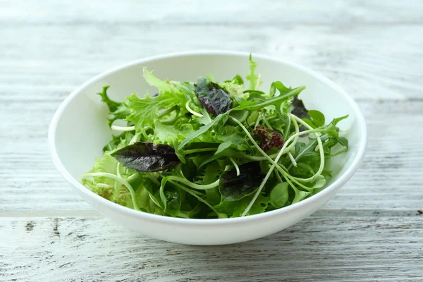 Fresh mixed green salad in bowl on wooden table close up — Stock Photo, Image