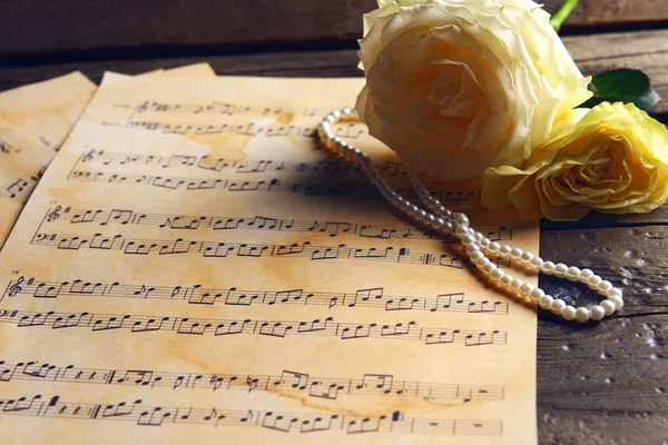 Όμορφα τριαντάφυλλα με μαργαριτάρια στα φύλλα της μουσικής στο ξύλινο τραπέζι, κινηματογράφηση σε πρώτο πλάνο — Φωτογραφία Αρχείου