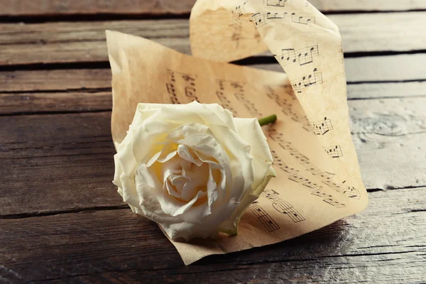 Beautiful rose wrapped on music sheet on wooden background — Stock Photo, Image